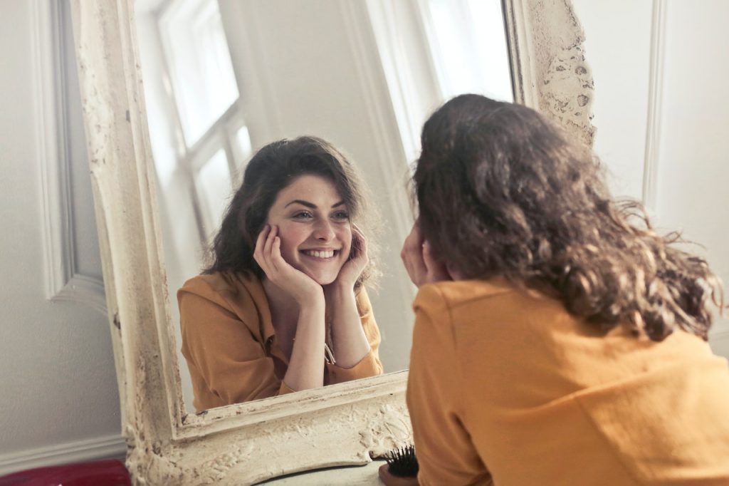 Woman with self-esteem smiling at herself in the mirror